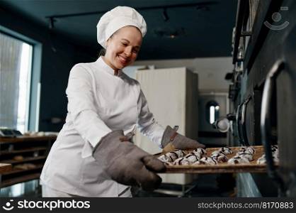 Happy smiling baker wearing white toque and jacket holding tray with cooked oatmeal cookies. Positive satisfied female chef taking hot fresh pastries out of oven. Happy smiling baker holding tray with cooked oatmeal cookies