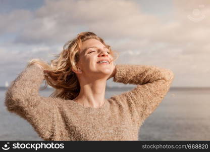 Happy smiling blonde woman portrait. Joyful female being positive walking outdoor wearing sweater having wind tousled hair in sunlight,. Happy woman outdoor wearing jumper