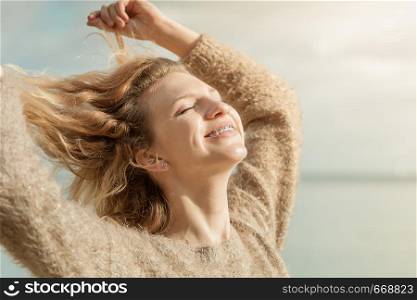 Happy smiling blonde woman portrait. Joyful female being positive walking outdoor wearing sweater having wind tousled hair in sunlight,. Happy woman outdoor wearing jumper