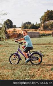 Happy smiling boy riding a bike, learning to ride a bike, in home garden. Real people, authentic situations