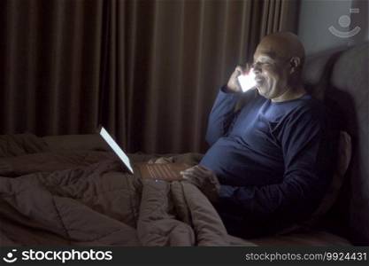 Happy smiling business, black man, African American people working from home and talking to colleagues on phone, video call conference in quarantine on bed in bedroom at home at late night. Lifestyle