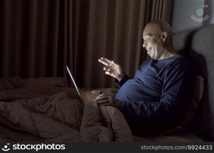 Happy smiling business, black man, African American people working from home and talking to colleagues in webcam video call conference with computer in quarantine in bedroom at home at late night.