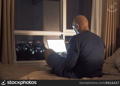 Happy smiling business, black man, African American people working from home and using computer notebook laptop with blank screen in quarantine on bed in bedroom at home at late night. Lifestyle