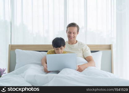 Happy smiling business blonde, man. Freelance working from home watching movie with his son with laptop computer notebook in quarantine. Family dad, children having fun together. Lifestyle.