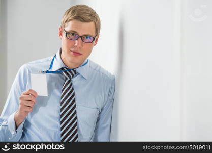 Happy smiling business man showing blank badge, while leaning on wall at office