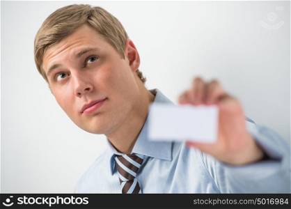 Happy smiling business man showing blank businesscard and dreaming, while leaning on wall at office