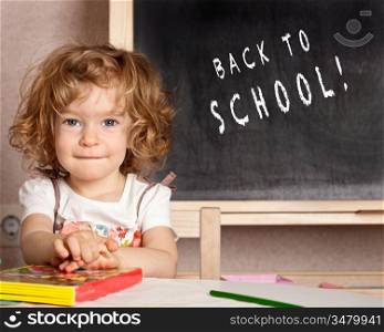 Happy smiling child in a class against blackboard with text &acute;Back to school!&acute;