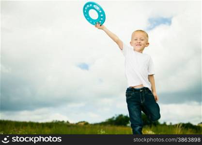 Happy smiling child in playground kid in action boy playing with blue frisbee disc. Active childhood