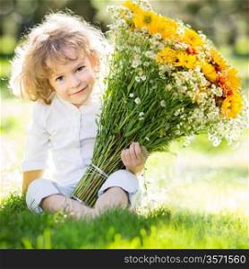 Happy smiling child with bouquet of spring flowers sitting on green grass outdoors