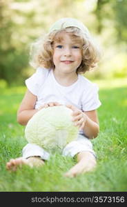 Happy smiling child with cabbage sitting on green grass in spring park. Healthy lifestyles concept