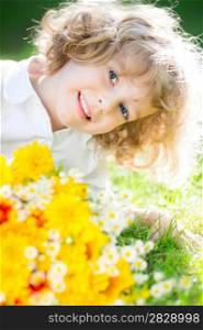 Happy smiling child with yellow spring flowers lying on green grass