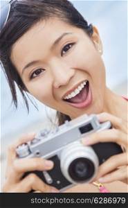 Happy smiling Chinese Asian young woman or girl in a bikini at the beach taking a photograph using a retro digital camera