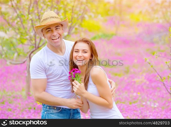 Happy smiling couple having fun in summer park, relaxation outdoors on pink floral glade, romance and love concept&#xA;