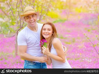 Happy smiling couple having fun in summer park, relaxation outdoors on pink floral glade, romance and love concept&#xA;