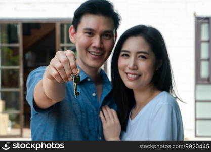 Happy smiling couple in front of the home and holding keys to New Home On Moving In Day, and start a new life family. Concept of homeowner and relocation