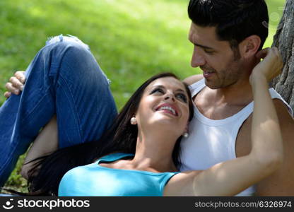 Happy smiling couple laying on green grass in a beautiful park