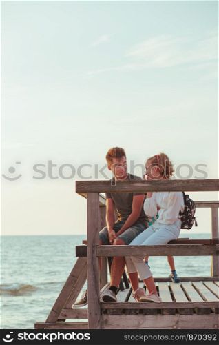 Happy smiling couple of young woman and man sitting on a pier over the sea during summer vacations. Copy space room for text