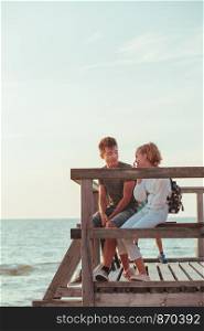 Happy smiling couple of young woman and man sitting on a pier over the sea during summer vacations. Copy space room for text
