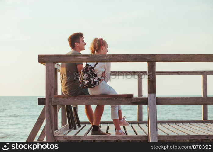 Happy smiling couple of young woman and man sitting on a pier over the sea during summer vacations. Copy space room for text