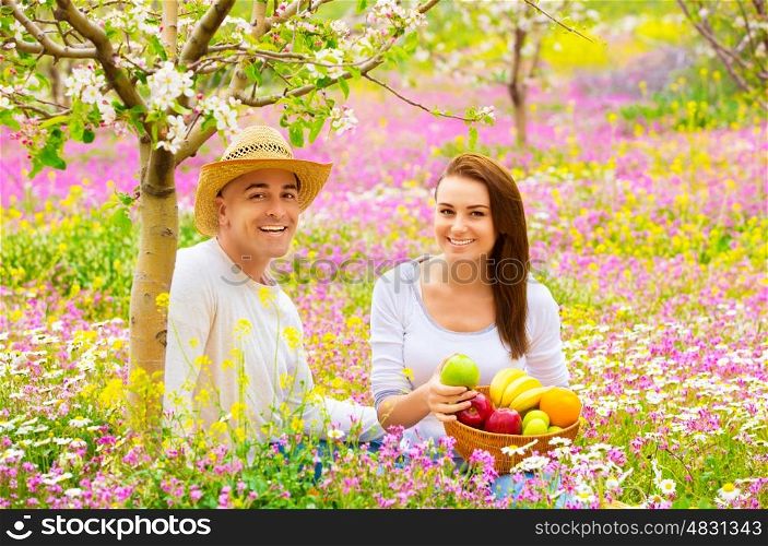Happy smiling couple on picnic in beautiful blooming garden, eating tasty fresh fruits, enjoying spring nature