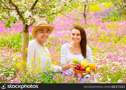 Happy smiling couple on picnic in beautiful blooming garden, eating tasty fresh fruits, enjoying spring nature