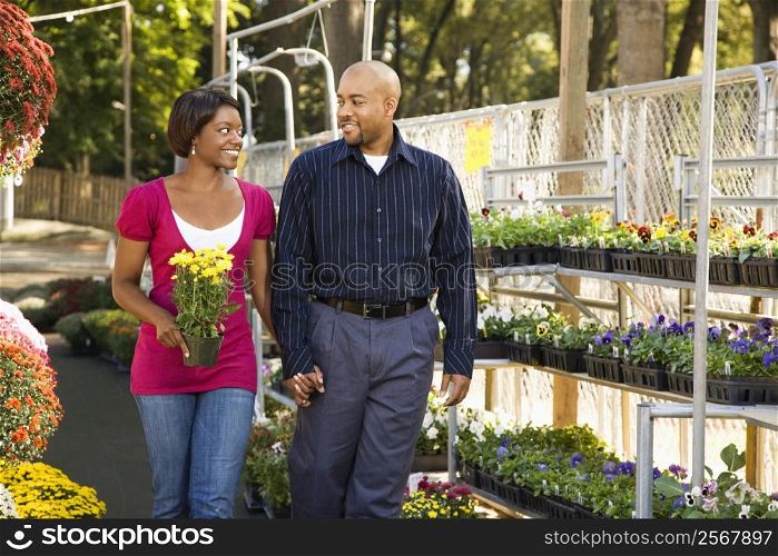 Happy smiling couple picking out flowers at outdoor plant market walking and holding hands.