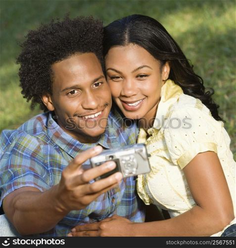 Happy smiling couple taking pictures together in park with digital camera.