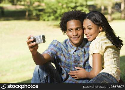 Happy smiling couple taking pictures together in park with digital camera.