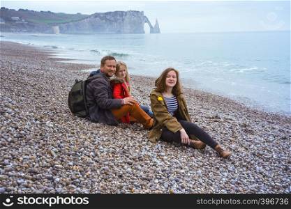 happy smiling dad and two daughters sitting on the beach of Etretat. France