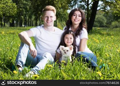 Happy smiling family of parents and daughter with pet dog in summer park. Family with pet dog in park