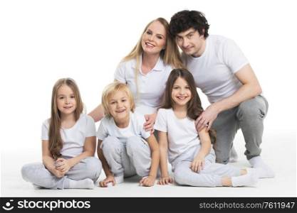 Happy smiling family of two parents and three children sitting on the floor studio isolated on white background. Family of parents and three children