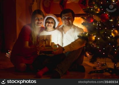 Happy smiling family sitting at fireplace and opening Christmas gift box