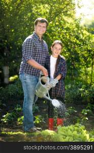 Happy smiling father and daughter watering garden bed at hot sunny day