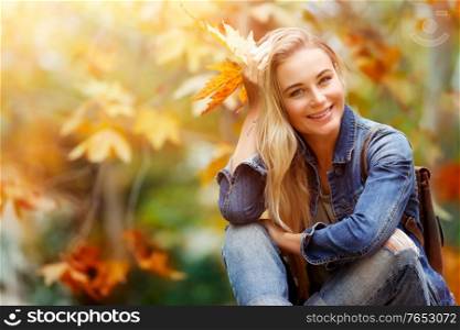 Happy smiling female sitting in autumn forest, enjoying last warm sunny autumnal days, spending fall vacation in the park