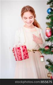 Happy smiling girl holding Christmas gift standing behinde a tree