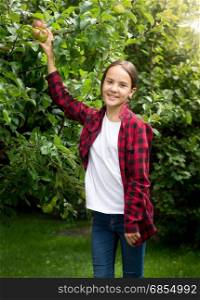 Happy smiling girl in red checkered shirt picking apples at garden
