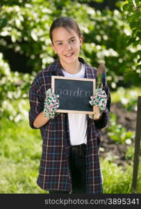 "Happy smiling girl in working clothes holding blackboard with word "Garden""