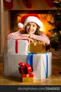 Happy smiling girl leaning on Christmas gift boxes at fireplace