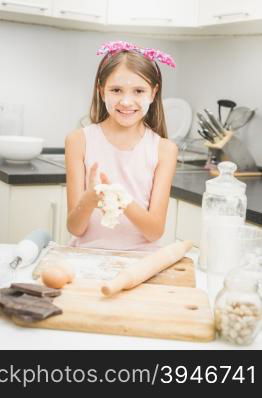 Happy smiling girl making dough for pie on kitchen