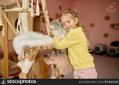 Happy smiling girl petting fluffy cat having fun time in animal shelter. Cheerful child hugging big fluffy kitten. Happy smiling girl petting fluffy cat having fun time in animal shelter