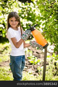 Happy smiling girl spraying small apple tree with fertilizers