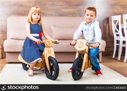 Happy smiling little children riding a wooden runbikes at home in the living room