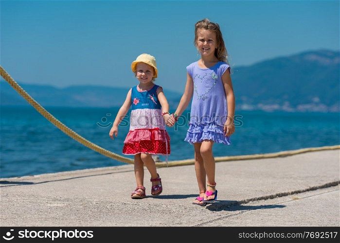 Happy smiling little sisters having fun holding their hands while walking on the beach coast during Summer vacation  Healthy childhood lifestyle concept