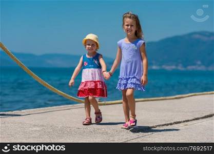 Happy smiling little sisters having fun holding their hands while walking on the beach coast during Summer vacation  Healthy childhood lifestyle concept