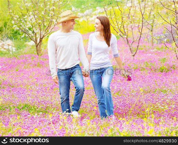 Happy smiling lovers holding hands and looking each other walking on pink floral field, enjoying family, romance and love concept