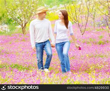 Happy smiling lovers holding hands and looking each other walking on pink floral field, enjoying family, romance and love concept