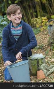 Happy smiling male boy child gardening with bucket, garden fork and watering can in a vegetable patch