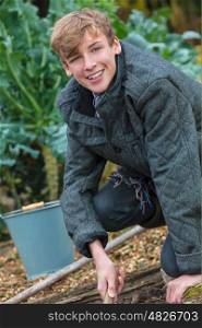 Happy smiling male boy child teenager young adult gardening with bucket and garden fork in a vegetable patch