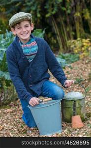 Happy smiling male boy child wearing hat or flat cap, gardening with bucket, garden fork and watering can in a vegetable patch