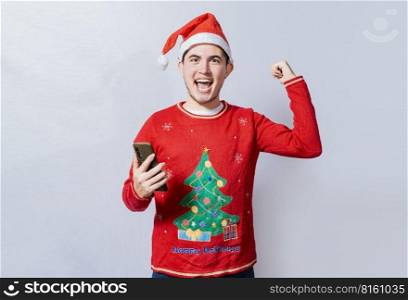 Happy smiling man in christmas hat holding cellphone celebrating, Happy guy in christmas hat holding cellphone celebrating, Teenager in christmas hat celebrating a promotion with the cell phone